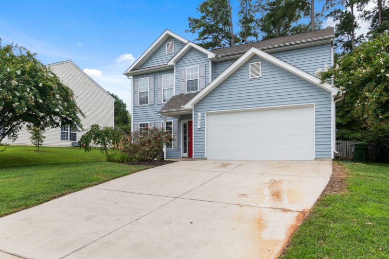 Home 31 Charming two-story suburban home with a spacious driveway surrounded by lush greenery.